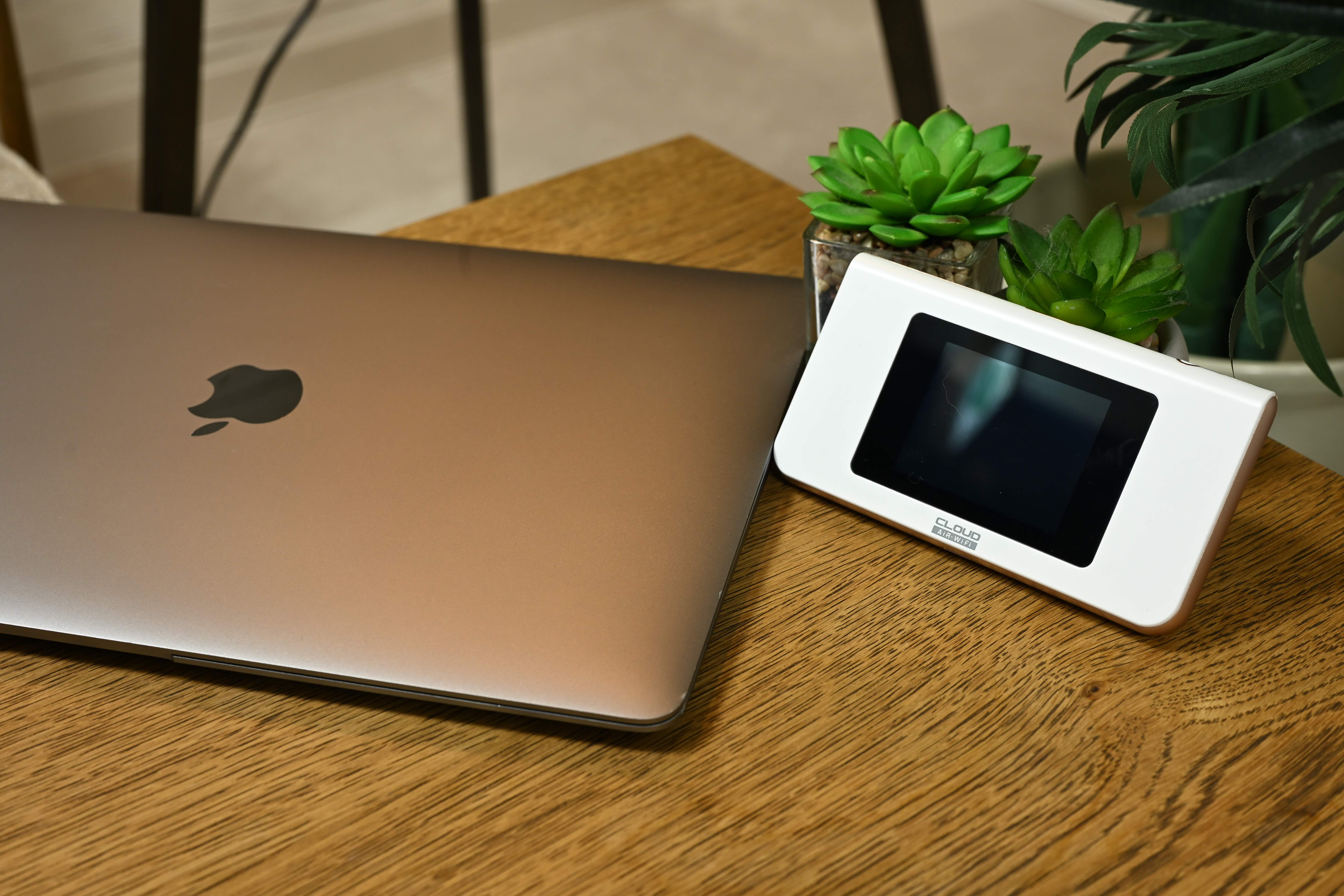 木製テーブルの上に置かれたAiR-WiFiのモバイルルーターとノートパソコン